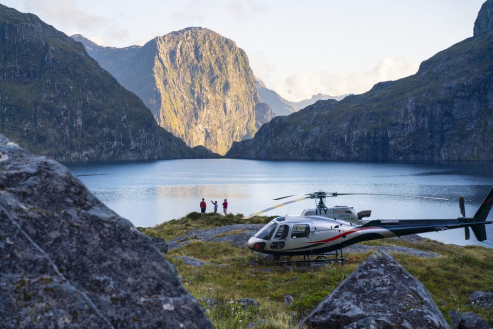 Landed Helicopter near lake with three people standing by the edge of the lake.