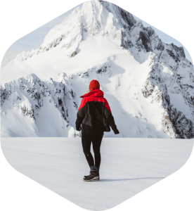 Women wearing red benie, red and black jacket and pants, standing in front of a snowy mountain.