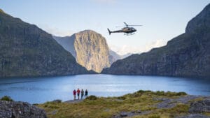 4 People standing at the edge of Lake Quill with a helicopter hovering above.
